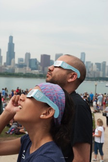 People with eclipse glasses looking up - Chicago skyline in bakground